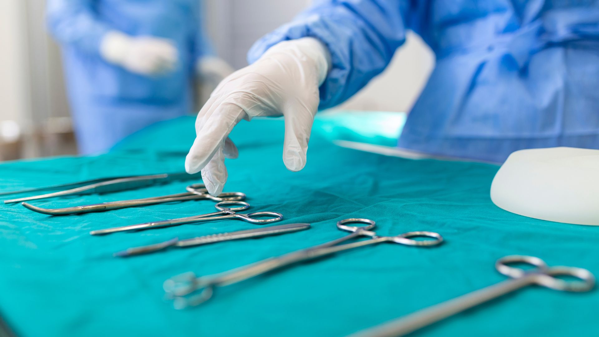 nurse hand taking surgical instrument for group of surgeons at background operating patient in surgical